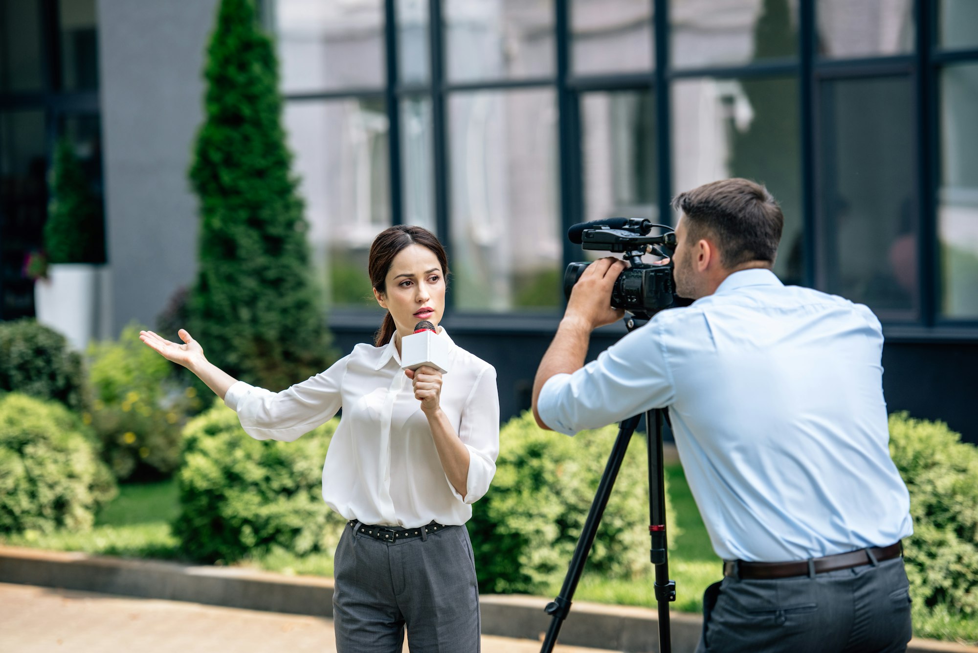 attractive journalist holding microphone and cameraman shooting her outside