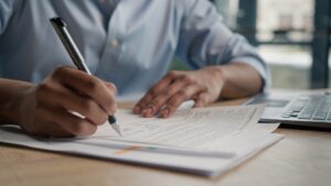 Close up unrecognizable man businessman writing paperwork report on desktop male hands signing